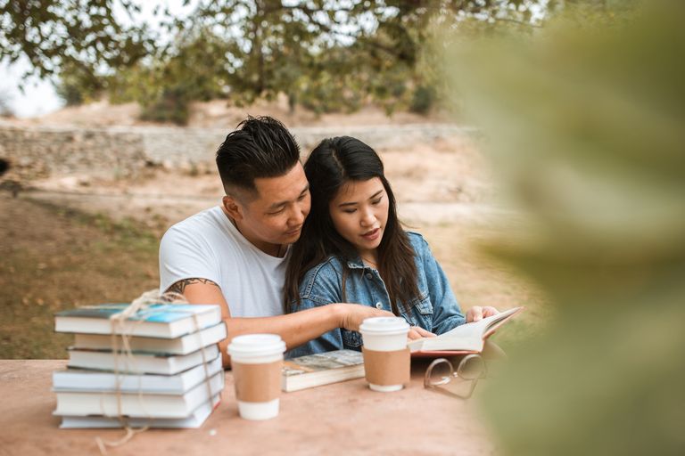 Asian couple reading Best Relationship Books together outdoors in a tranquil setting, conveying love and relaxation.