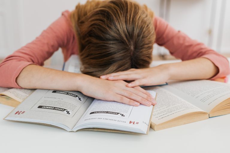 A student overwhelmed by studying falls asleep on open books at a desk, representing academic fatigue and high-achieving kids burn out.